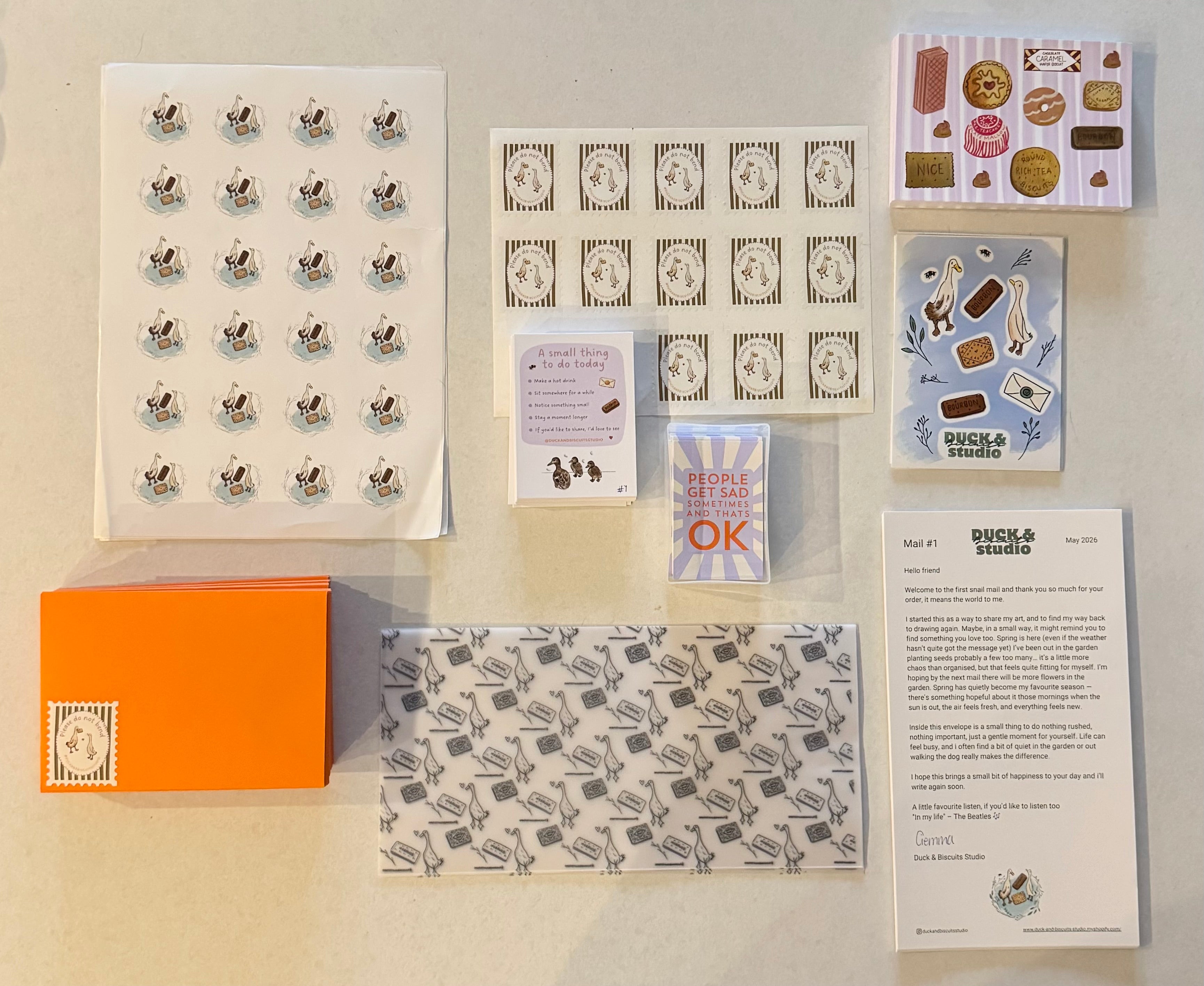 Collection of stationery items including cards, stickers, and an orange box on a beige background