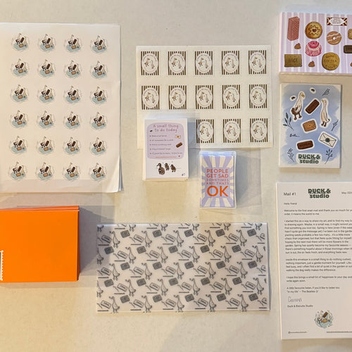 Collection of stationery items including cards, stickers, and an orange box on a beige background